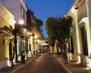 A narrow street lined with buildings, trees, and street lamps. - Hotel La Siesta Malecón (Mazatlán)