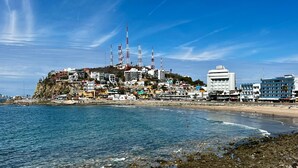 A coastal town with buildings on a cliff, a beach, and rocky shoreline. - Hotel La Siesta Malecón (Mazatlán)