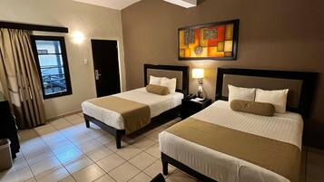 A hotel room with two beds, a nightstand with a lamp, a painting on the wall, and a window with curtains.