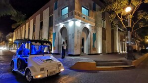 A white car with blue interior lights parked in front of a building with a balcony and arched entrance. - Hotel La Siesta Malecón (Mazatlán)