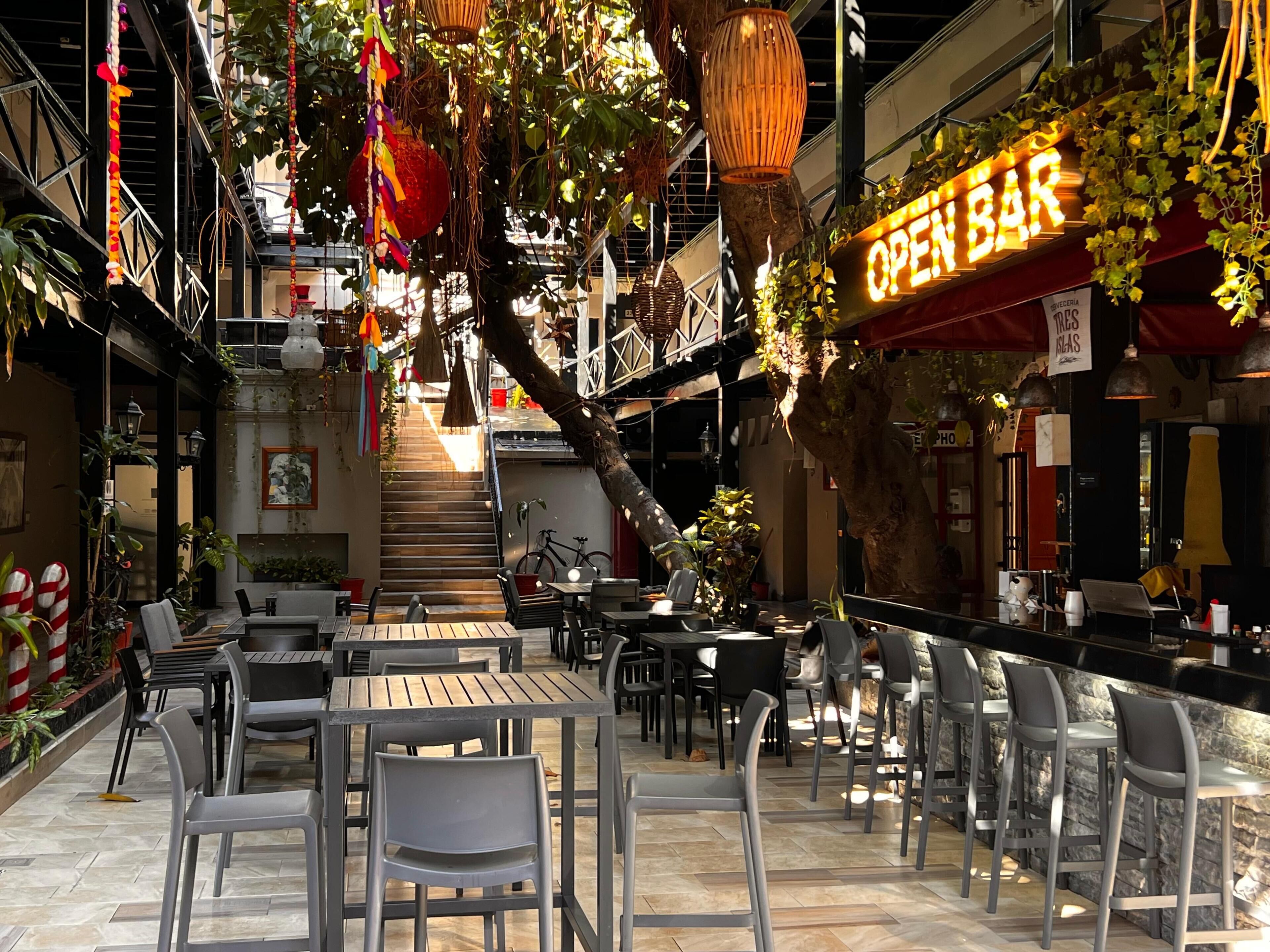 Un café al aire libre con mesas y sillas, una escalera y un letrero que dice 'OPEN BAR'.