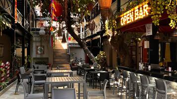 Un café al aire libre con mesas y sillas, una escalera y un letrero que dice 'OPEN BAR'.