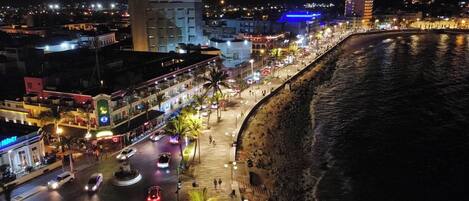 A coastal cityscape at night with a beach promenade, streetlights, and buildings along the waterfront.
