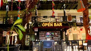 An indoor bar with a sign reading "OPEN BAR", tables and chairs arranged for seating, and a variety of bottles on shelves. - Hotel La Siesta Malecón (Mazatlán)