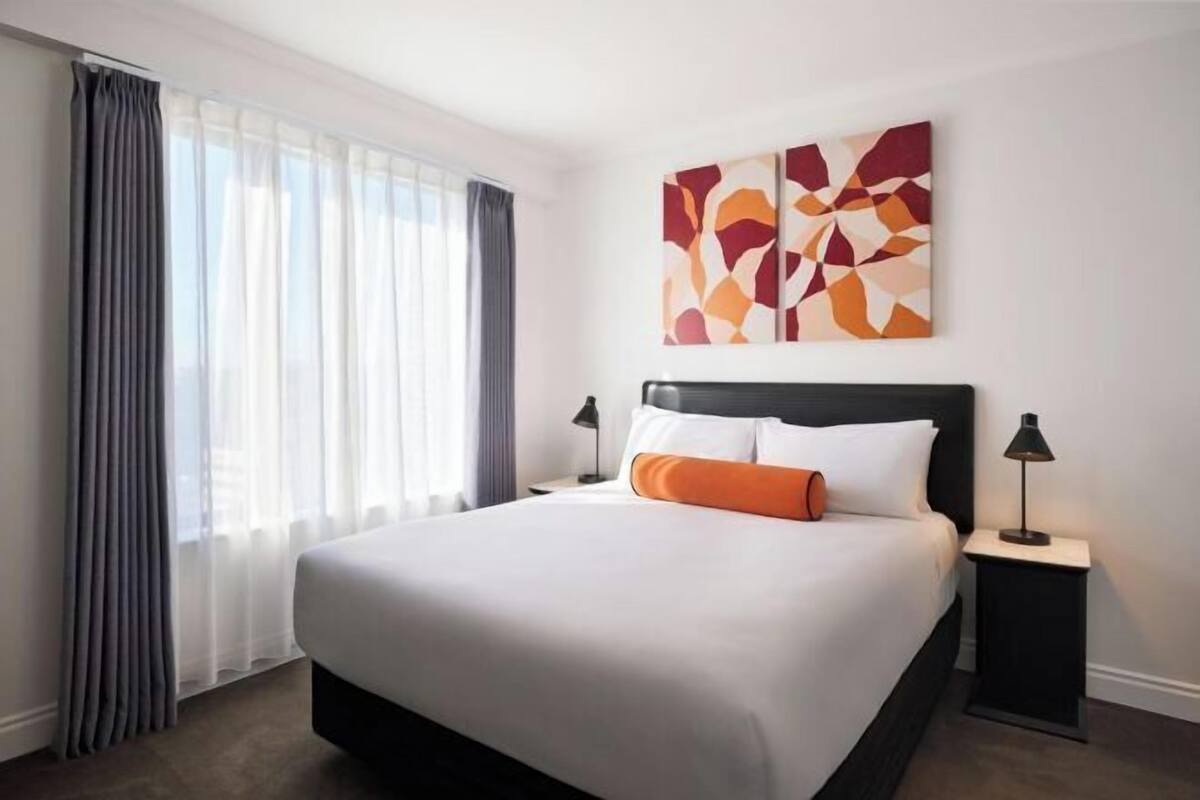 A hotel room with a large bed, a nightstand, a lamp, and a window with curtains.
