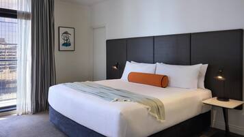 A hotel room with a large bed, a nightstand, a framed picture on the wall, and a view through the window.