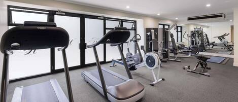 Une salle de sport équipée de tapis de course, d’appareils de musculation et d’un mur recouvert de miroirs.