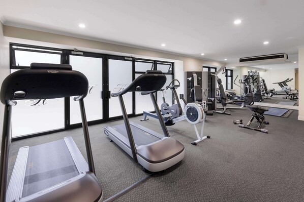 A gym with treadmills, weight machines, and a mirrored wall.