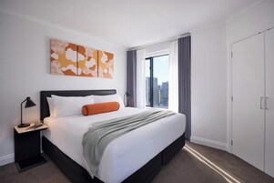Ein modernes Hotelzimmer mit einem großen Bett, einem Nachttisch, einem Fenster mit Vorhängen und Blick auf die Stadt.