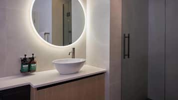 Un baño con un espejo redondo, un lavamanos blanco y dos botellas de jabón para manos.