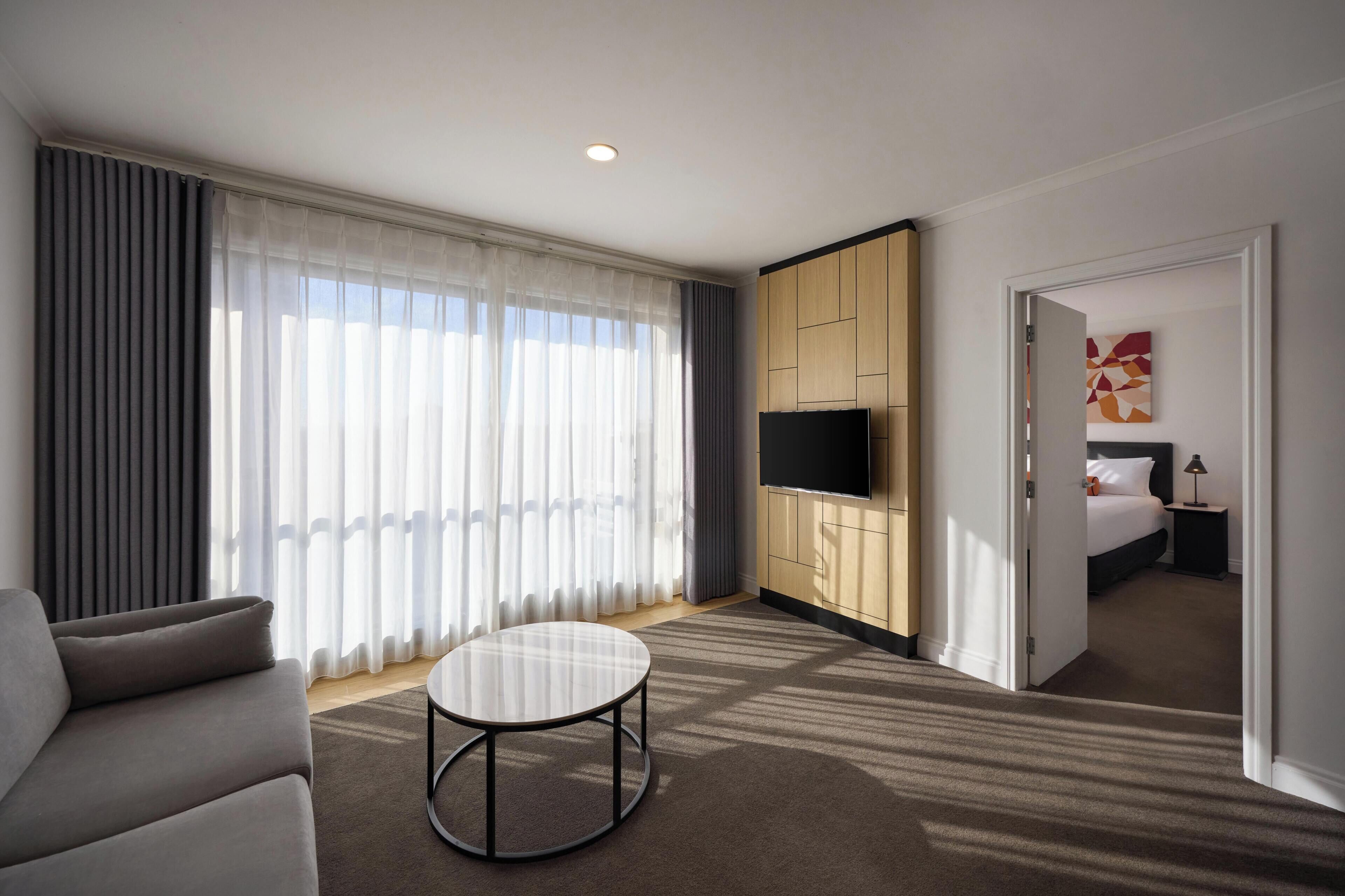 Habitación de hotel con sofá, una mesa redonda, televisión, cama y un cuadro en la pared.