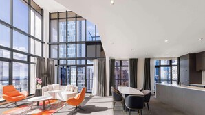 A modern hotel room with a large window, a sofa, a dining table, and a kitchen area. - Adina Citylife Auckland (Auckland)