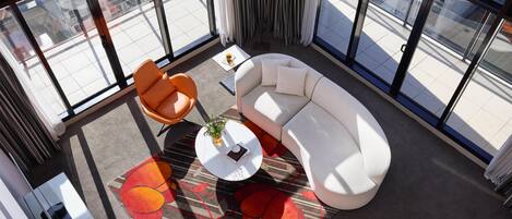 A modern room with a white sofa, orange chairs, a small table with a plant, and a patterned rug.
