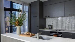 A modern kitchen with grey cabinetry, a white countertop, a built-in oven, and a large window with a view of buildings. - Adina Citylife Auckland (Auckland)