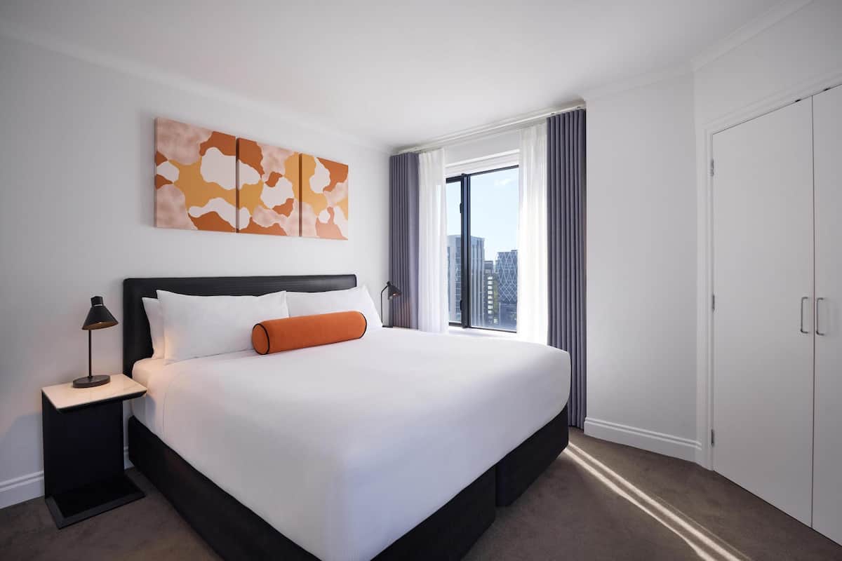 A hotel room with a large bed, a nightstand, a window with curtains, and a city view.