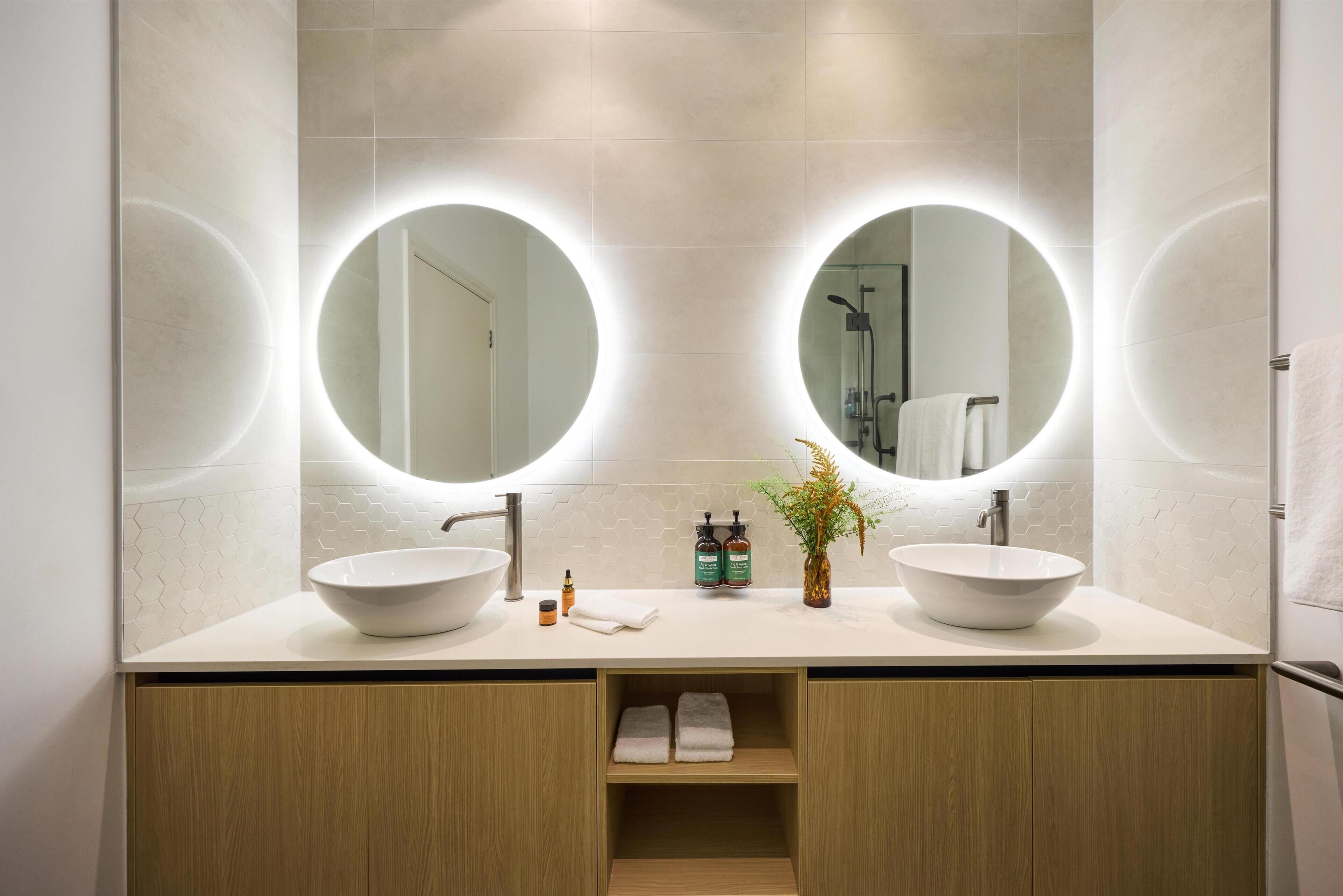 A modern bathroom with two sinks, round mirrors, and a wooden cabinet.