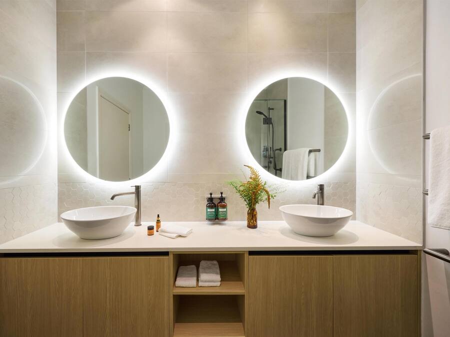 A modern bathroom with two sinks, round mirrors, and a wooden cabinet.