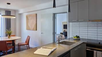 Uma cozinha moderna com bancada de mármore, área de jantar com mesa e cadeiras, e vista para o cômodo adjacente.