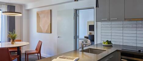 A modern kitchen with a marble countertop, a dining area with a table and chairs, and a view into the adjacent room.