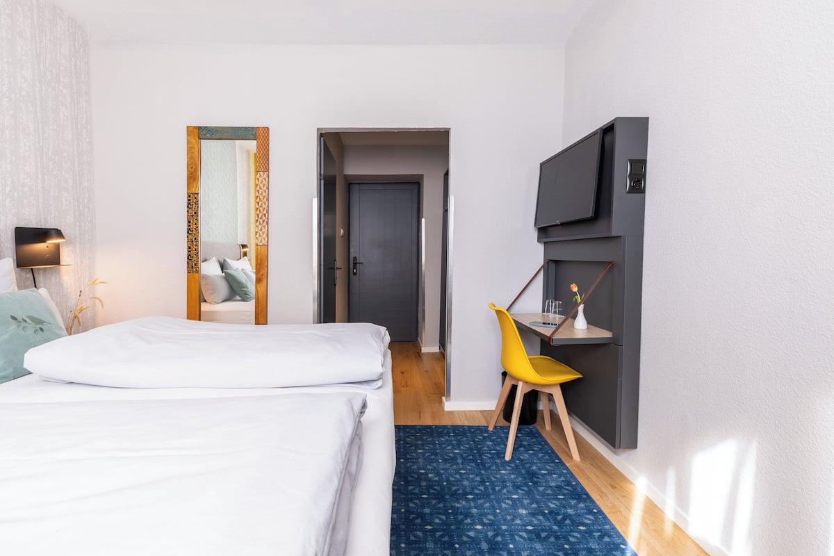 A hotel room with a bed, a desk with a chair, a TV, and a mirror.