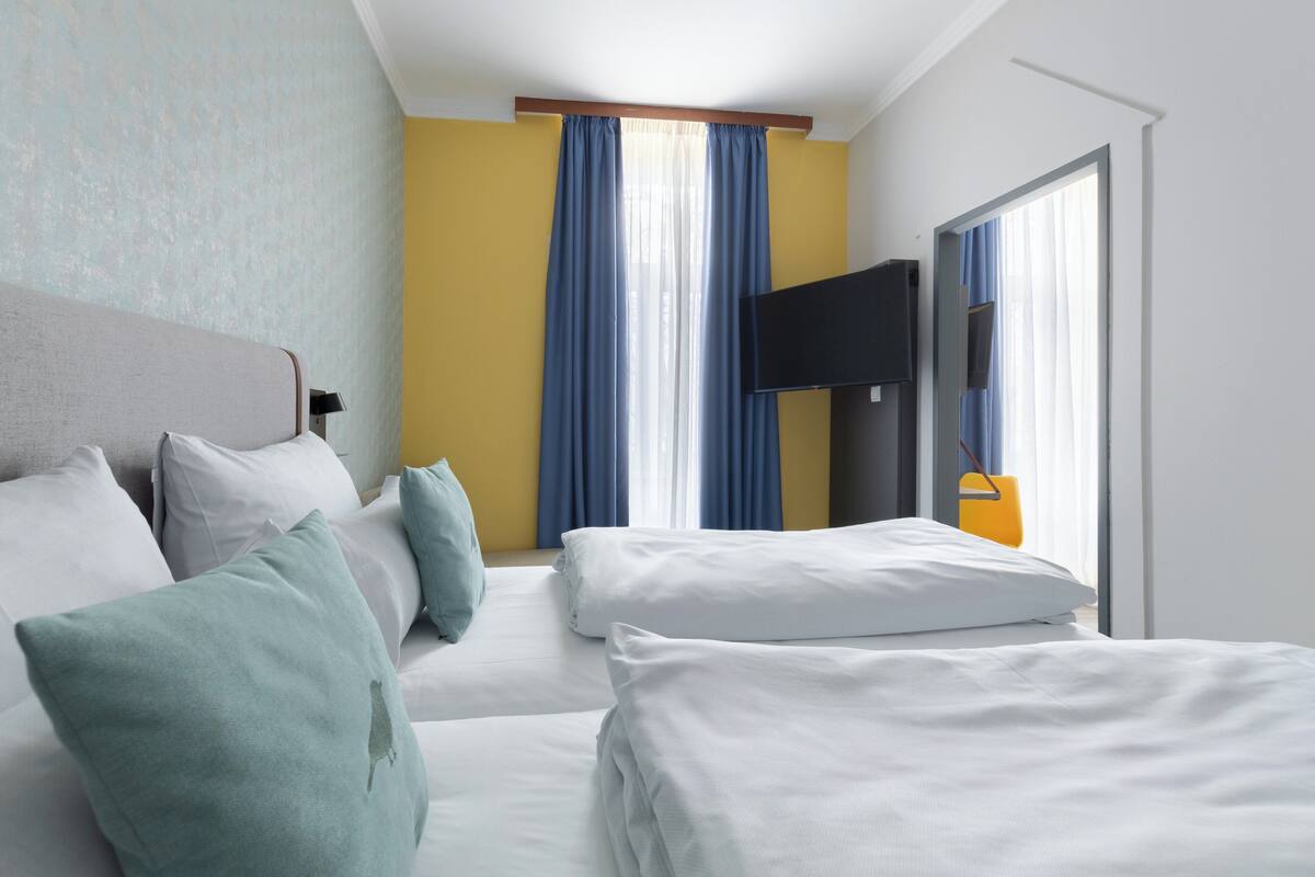 A hotel room with two beds, a flat-screen TV, and a large window with curtains.