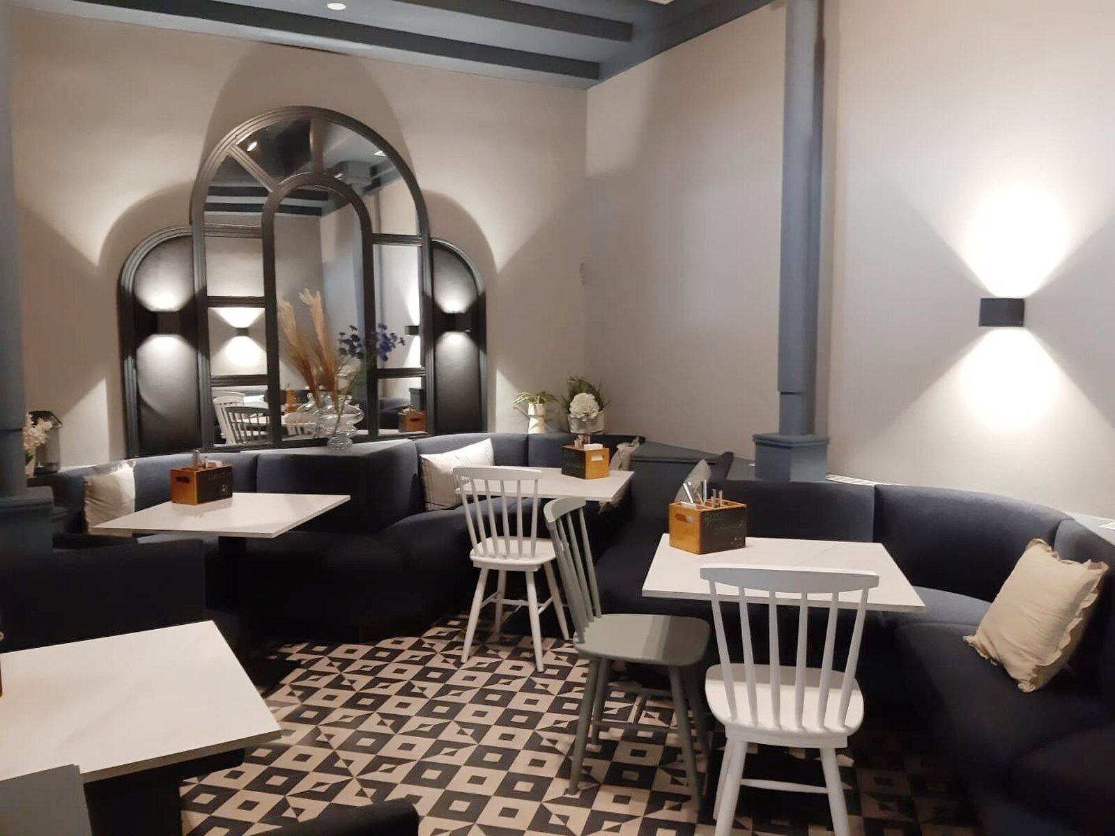 A modern dining area with a geometric patterned floor, black and white furniture, and a large mirror above the seating area.