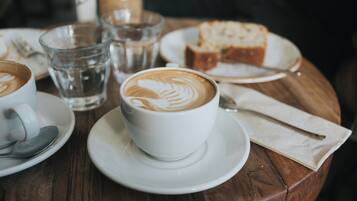 A table with a cup of coffee, a glass of water, a slice of bread, and a spoon.