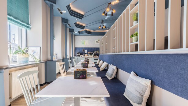 Un comedor moderno con una mesa larga, sillas blancas, un banco acolchado azul e iluminación colgante.