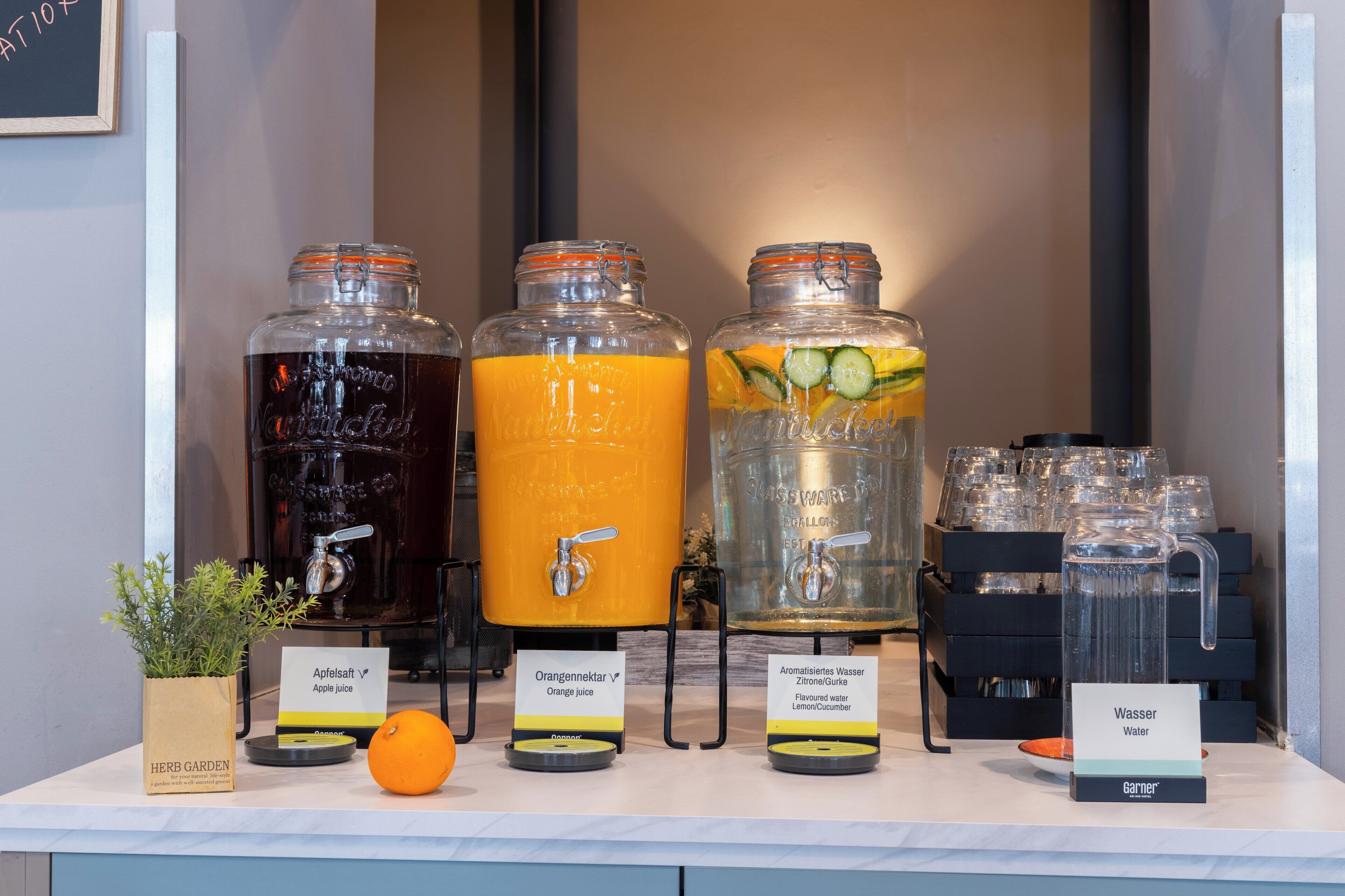 A beverage station with three dispensers, one for apple juice, one for orange juice, and one for lemon/cucumber water.