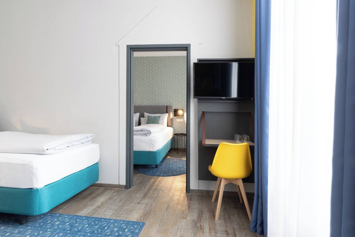 A hotel room with two beds, a TV, a yellow chair, and a small table.