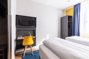 A modern hotel room with a bed, a TV mounted on the wall, a small desk with a chair, and a wardrobe. - Garner Hotel Vienna by IHG (Vienna)