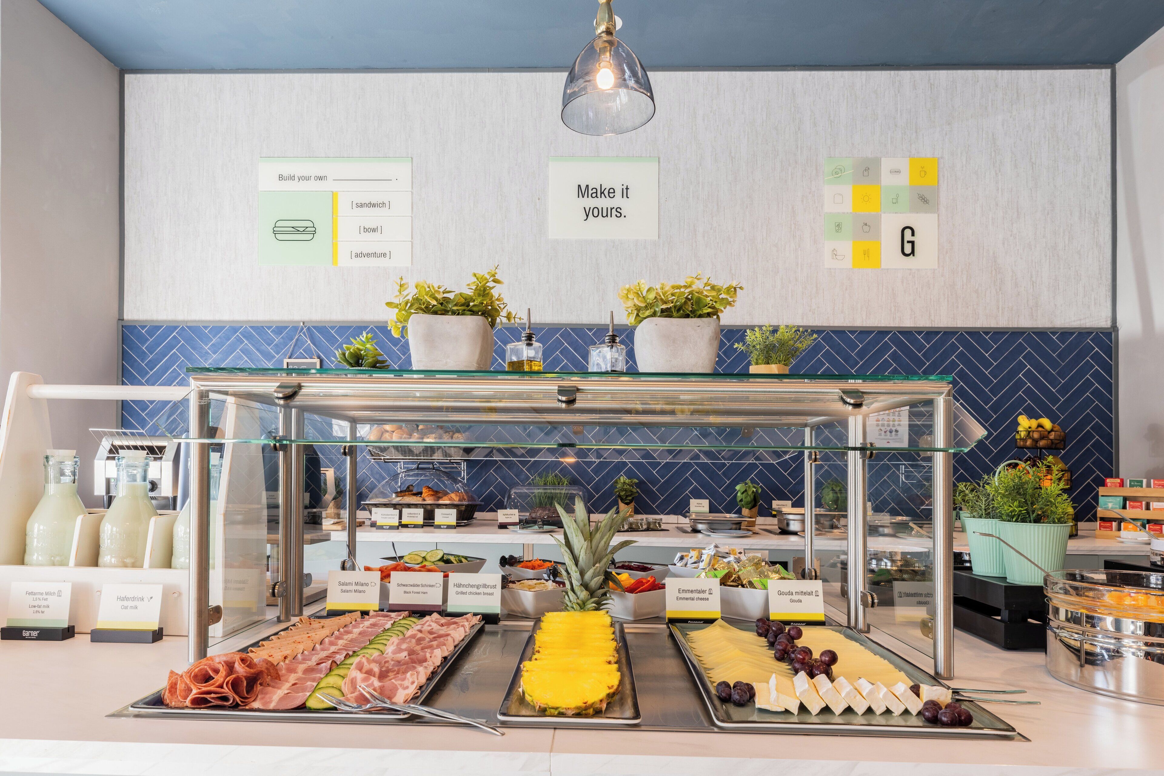 Een buffet met diverse etenswaren, waaronder vlees, kazen en fruit, met een bord waarop staat: “Maak het jouw eigen.”