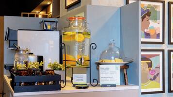 Un espacio para bebidas con un dispensador grande de agua, una máquina de café y una selección de bebidas embotelladas.