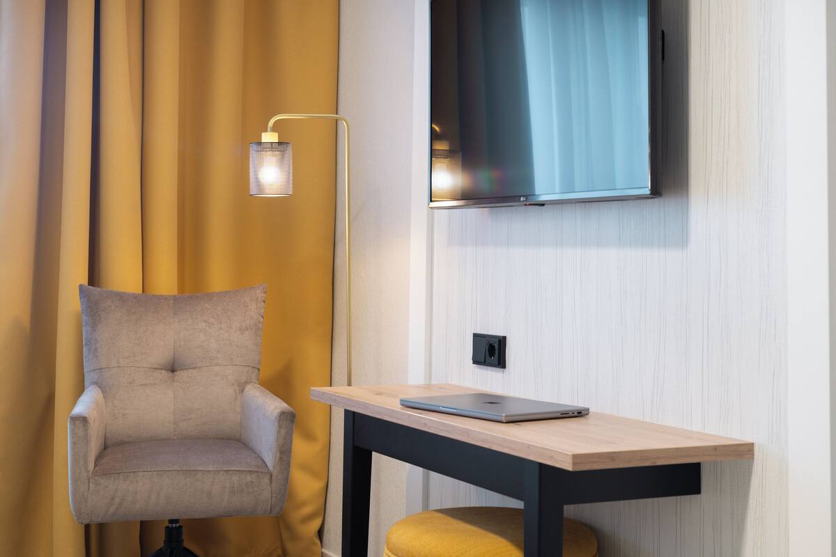 A modern room with a sofa, a table with a laptop, a TV mounted on the wall, and a floor lamp.