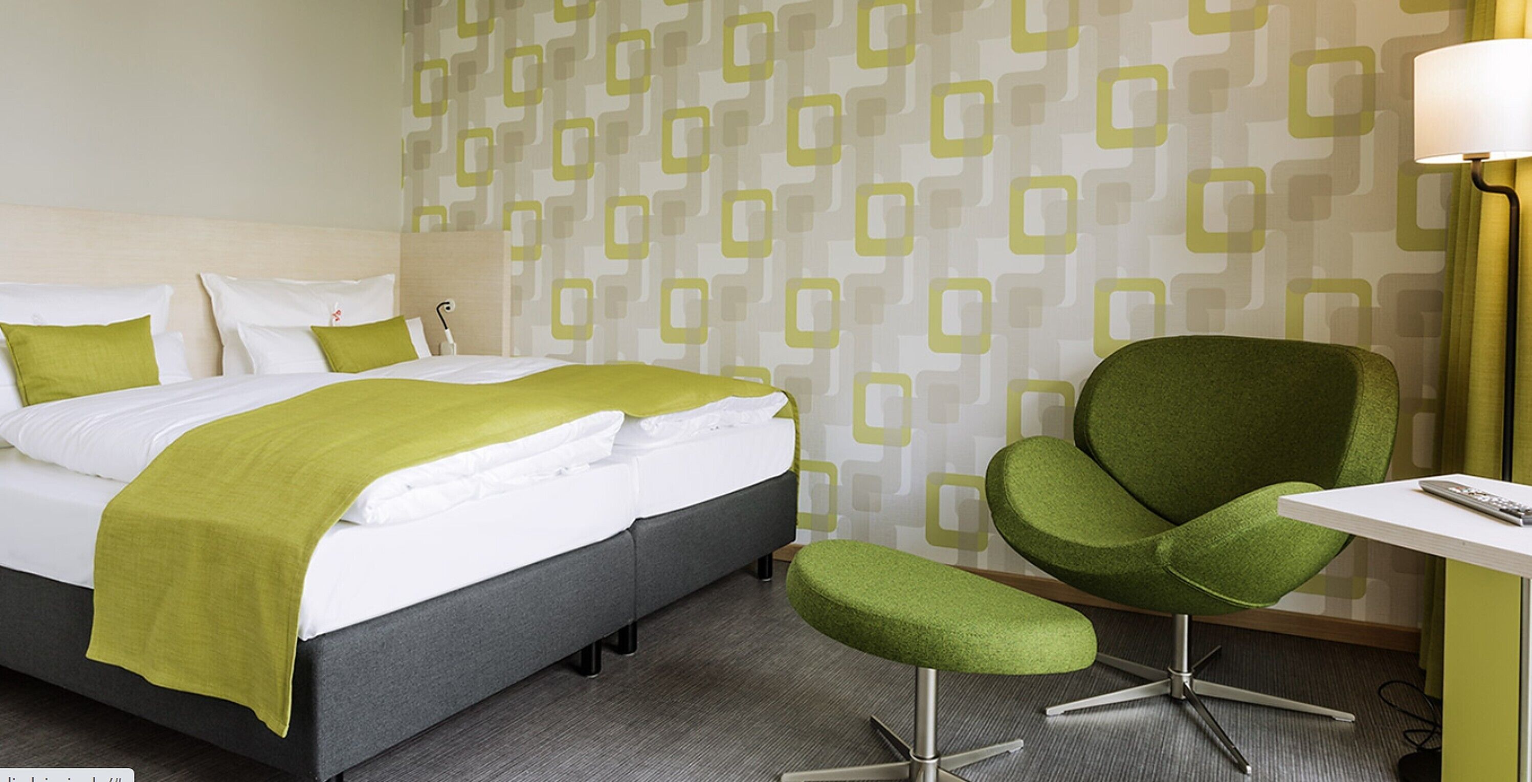 A hotel room with a bed, a green armchair, a small table, and a lamp.