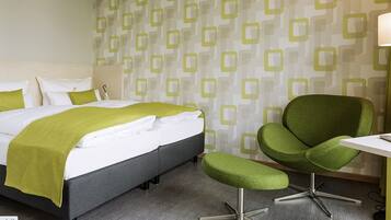 A hotel room with a bed, a green armchair, a small table, and a lamp.