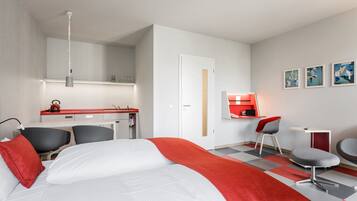 A hotel room with a bed, a desk, a chair, a small table, and a red and grey checkered floor.