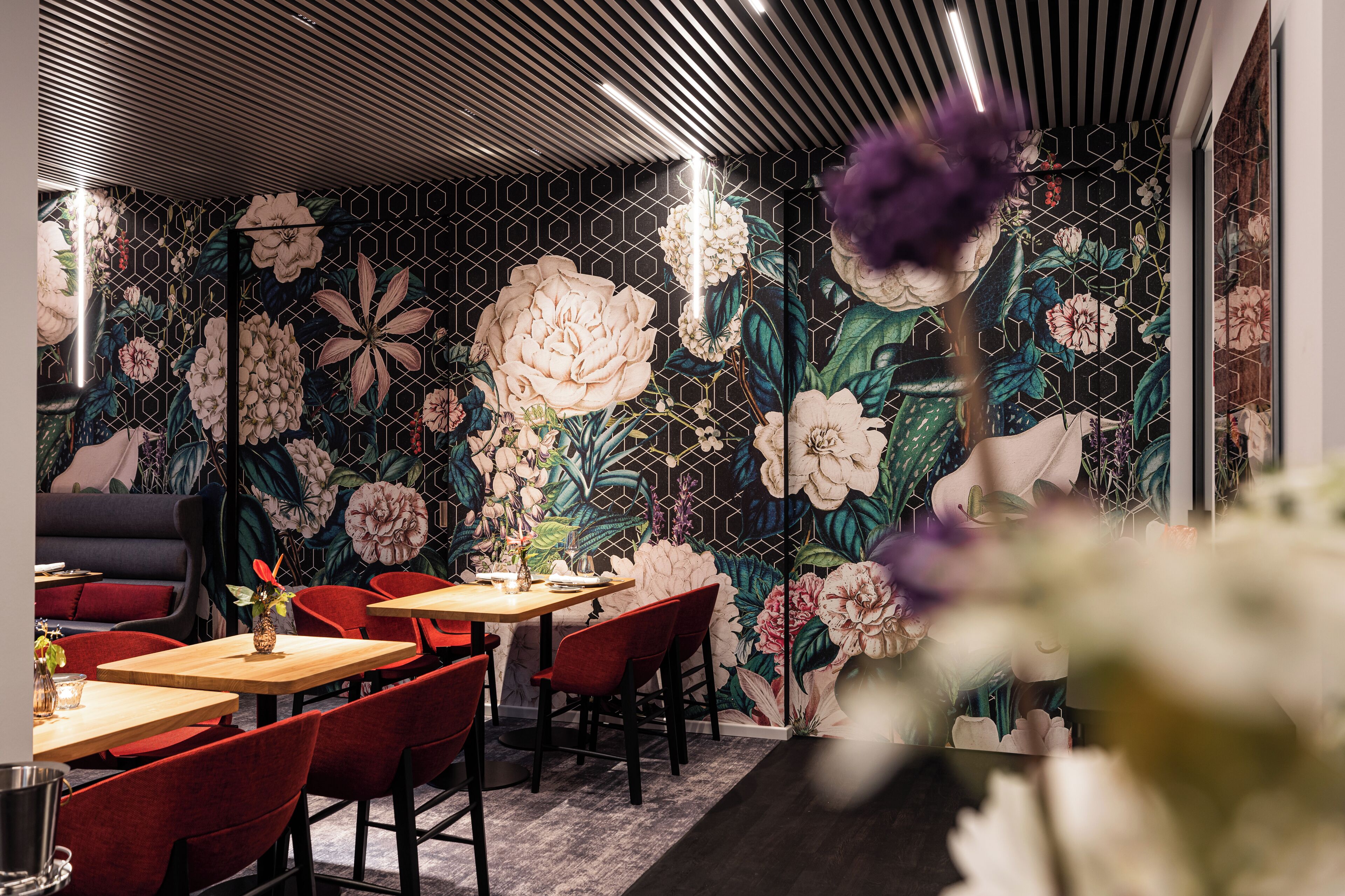 A restaurant with a floral wall mural, red chairs, and wooden tables.