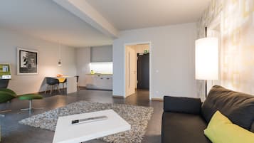 A modern living room with a grey sofa, a white coffee table, and a green chair. There is a kitchen area in the background with a yellow countertop.