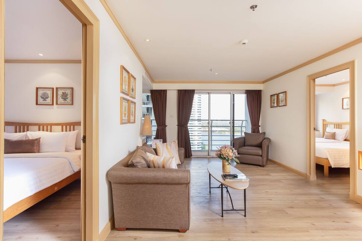 A spacious hotel room with a bed, a sofa, a coffee table, and a view of the city.