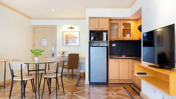 A compact kitchen with a refrigerator, microwave, and a flat-screen TV. There is a dining area with a table and chairs, and a small potted plant on the table.
