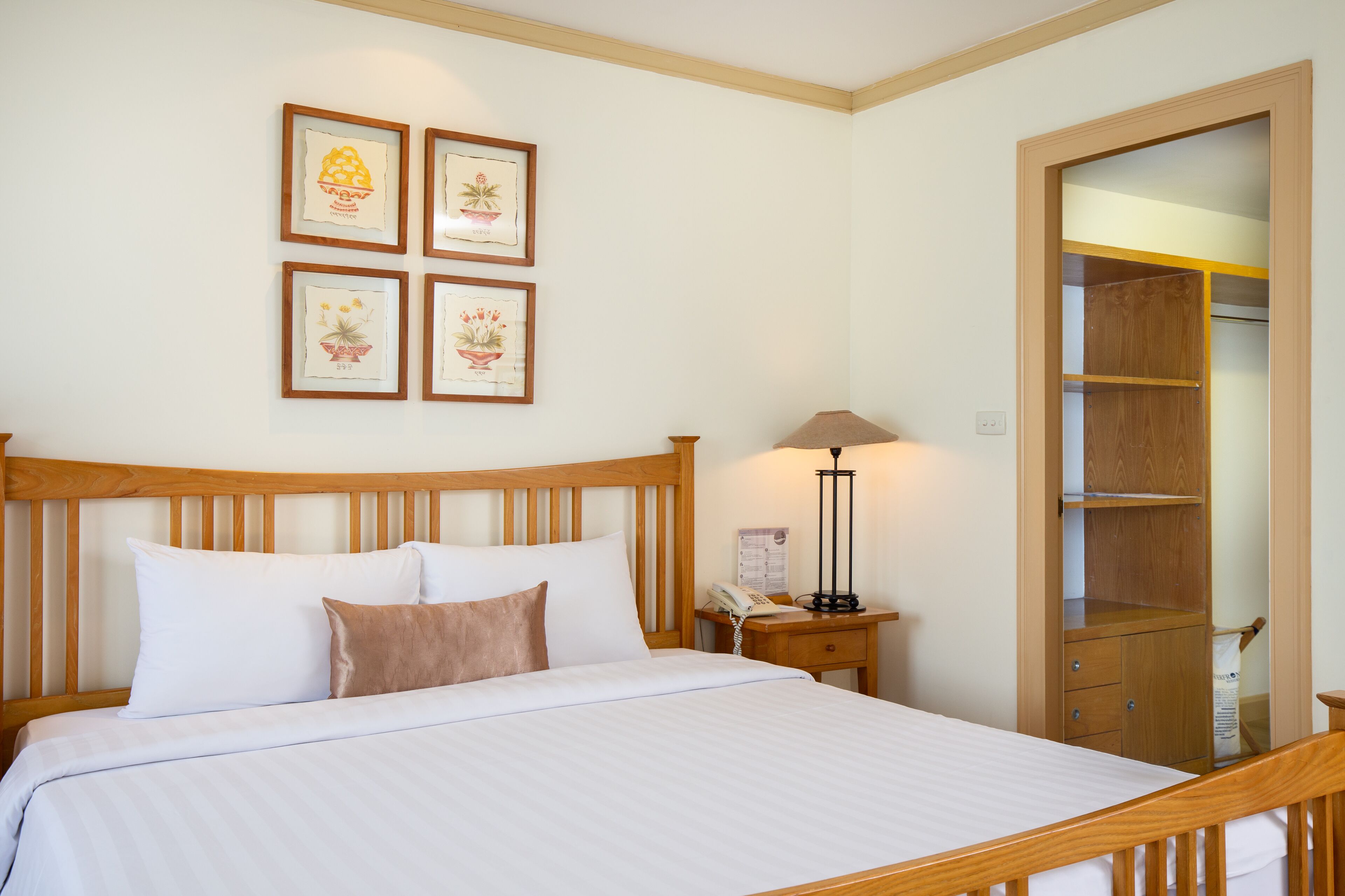 A neatly made bed with white and brown bedding, a wooden headboard, a bedside table with a lamp, and a wooden wardrobe with a mirror.