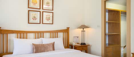 Una cama bien hecha con ropa de cama blanca y marrón, un cabecero de madera, una mesita de noche con una lámpara y un armario de madera con espejo.