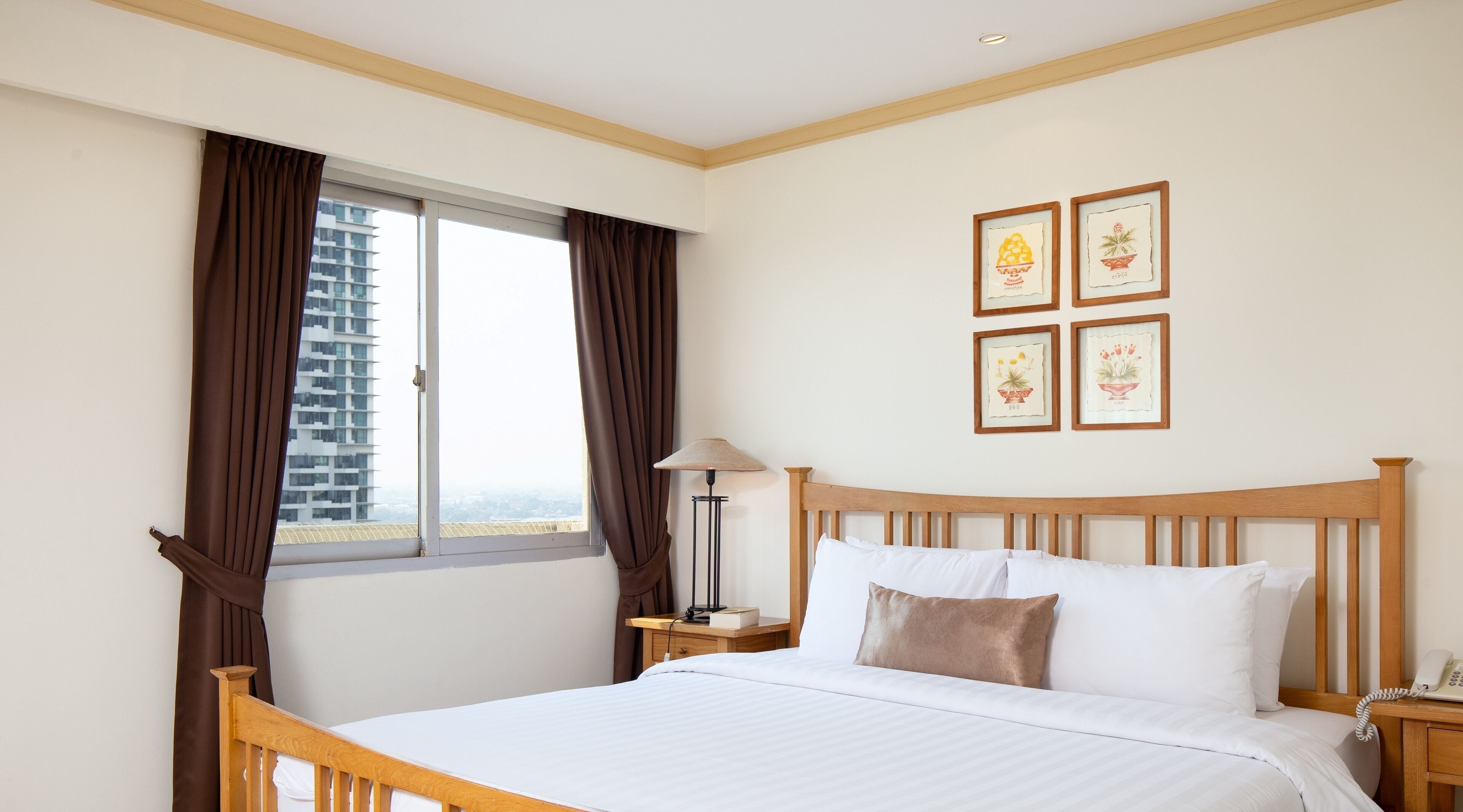 A hotel room with a bed, a nightstand, a lamp, a window with curtains, and four framed pictures on the wall.
