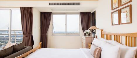 Habitación de hotel con una cama grande, un sofá, un escritorio con lámpara y vistas a la ciudad desde la ventana.