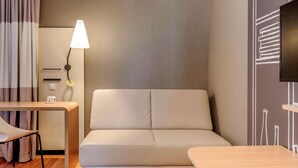 Een moderne hotelkamer met een bank, een tafeltje, een lamp en een aan de muur bevestigde televisie.