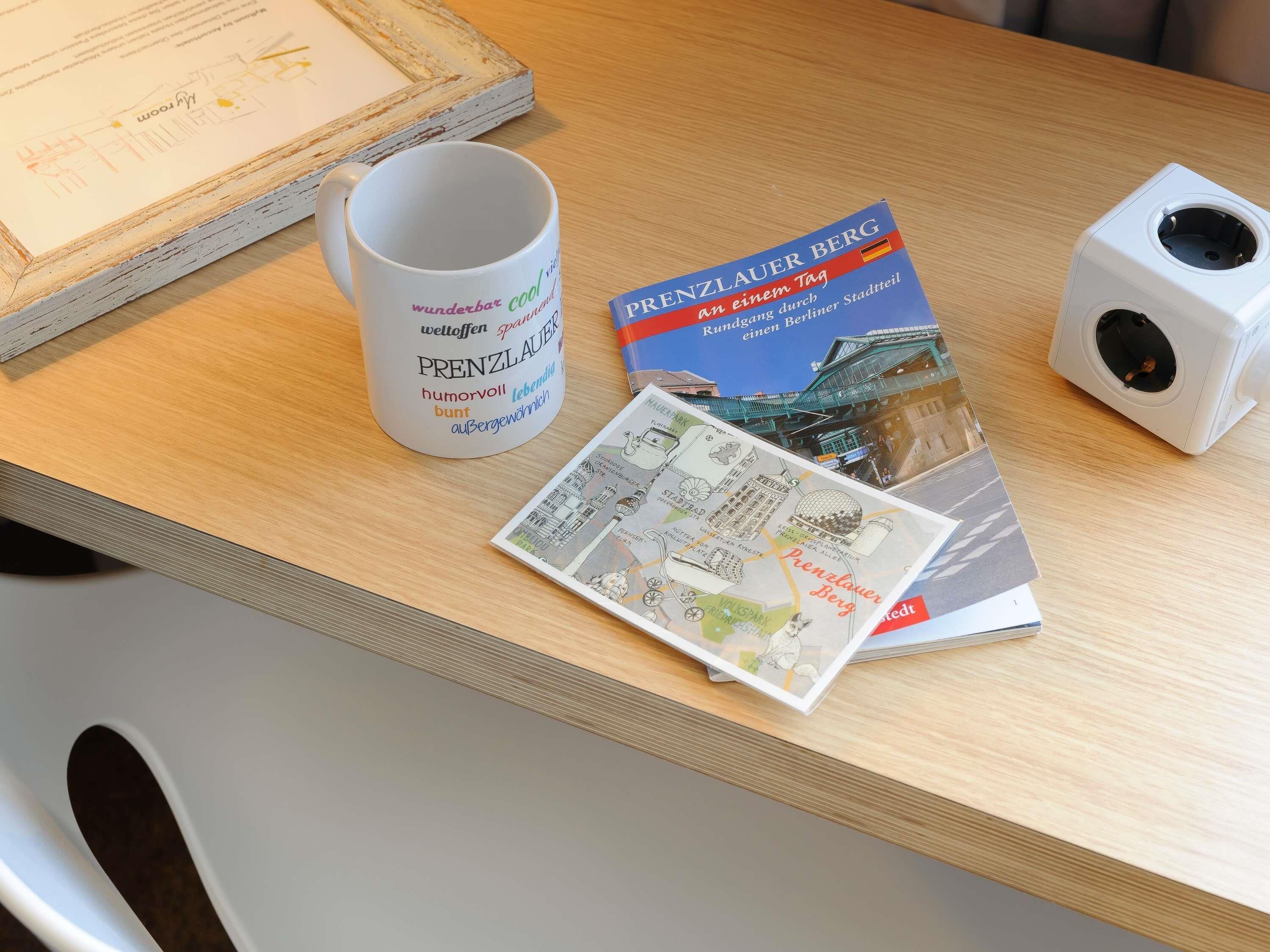 A table with a white mug, a brochure titled 'Prenzlauer Berg', and a white speaker.