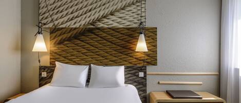 A neatly arranged hotel room with a bed, bedside table, and a laptop on the table.
