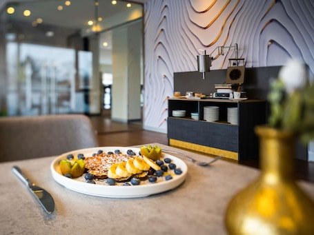 A breakfast setting with a plate of pancakes, blueberries, and sliced bananas.. ibis Berlin Mitte