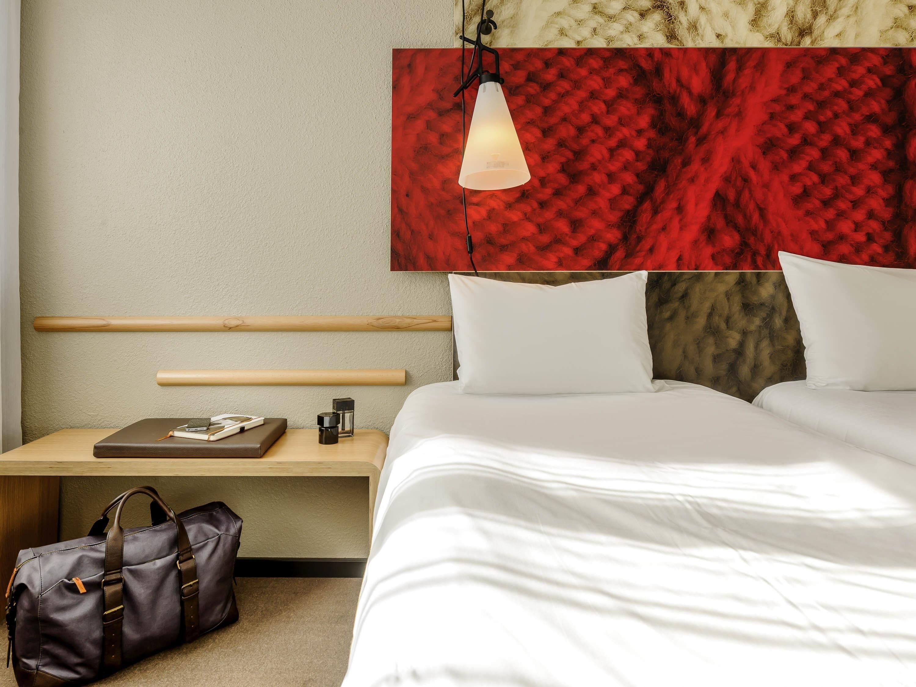 A hotel room with a bed, bedside table, lamp, and a red textured wall.